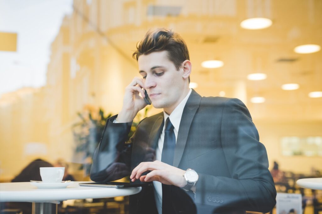 Portrait of young businessman sitting in cafe using digital tablet and mobile phone.